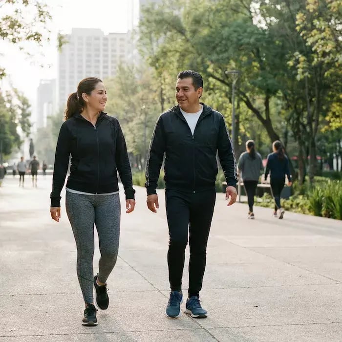 dos adultos mexicanos (hombre y mujer) de complexión promedio caminando activamente en un parque urbano mexicano contemporáneo por la mañana.